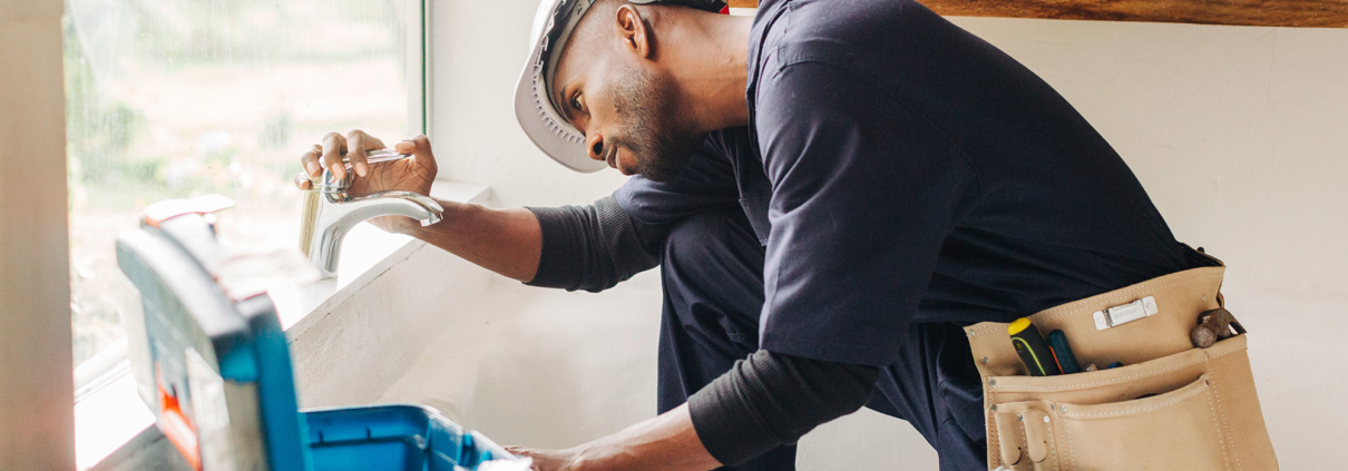 Homme accroupi avec un coffre à outil faisant de l'entretien d'une conduite de plomberie